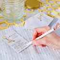 Hand writing on a card with a glass jar and decorative elements in the background