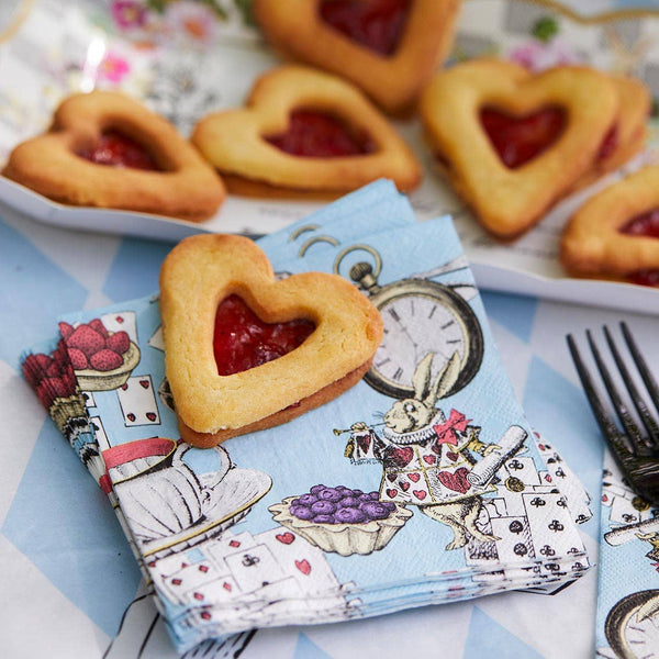 Heart-shaped cookies with jam filling on a decorative napkin with Alice in Wonderland design.