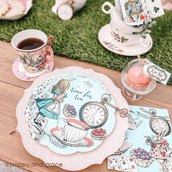 Tea party setup with Alice in Wonderland theme, including teacups, plates, and a clock.