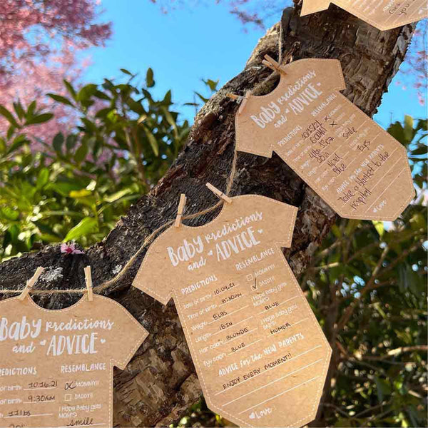 Kraft paper baby onesie-shaped cards with predictions and advice on a tree branch.