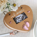 Heart-shaped photo album with ultrasound inside, surrounded by flowers on a light surface