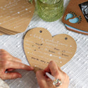 Heart-shaped baby predictions and advice card being filled out with a pen on a textured surface.
