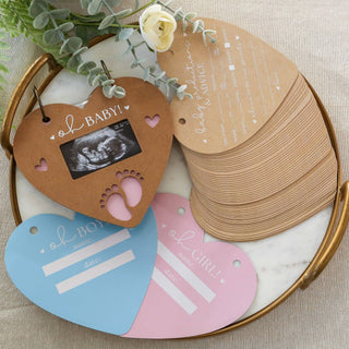 Heart-shaped baby announcement tags with ultrasound photo on a marble tray.