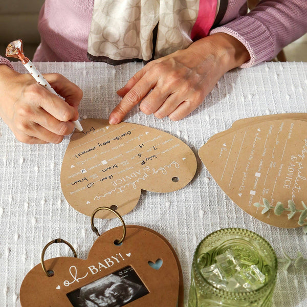 Two people writing on heart-shaped paper with a glass of water on a table.