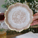 Decorative plate with lace design held by a hand, with a blurred background of a table setting.