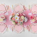 Heart-shaped pink plates with floral centerpieces on a pink background