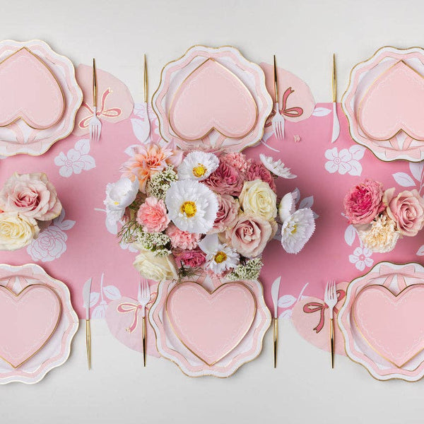 Heart-shaped pink plates with floral centerpieces on a pink background