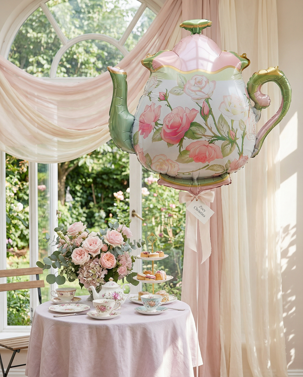 Decorative floral teapot on a table with tea set and flowers in a sunlit room.