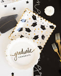 Graduation-themed party supplies including plates, napkins, and a balloon on a black and white background.