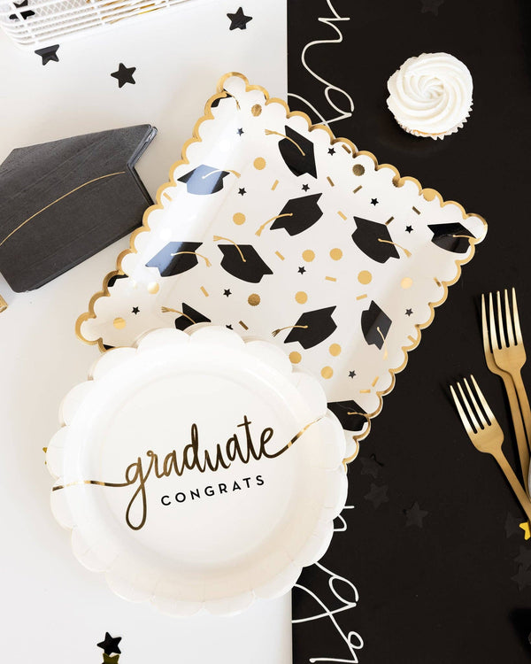 Graduation-themed party supplies including plates, napkins, and a balloon on a black and white background.