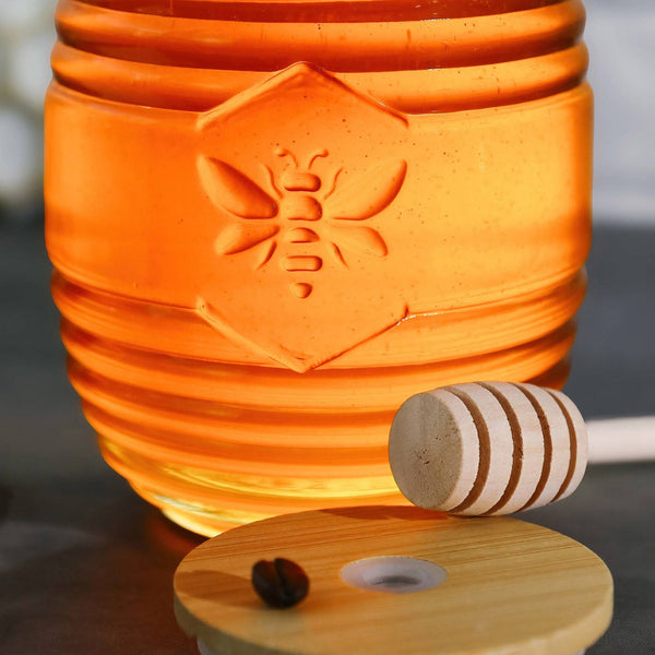 Orange ceramic honey jar with a wooden honey dipper on a reflective surface