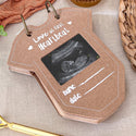 Brown photo album with ultrasound image and 'Love at first heartbeat' text on a textured surface.