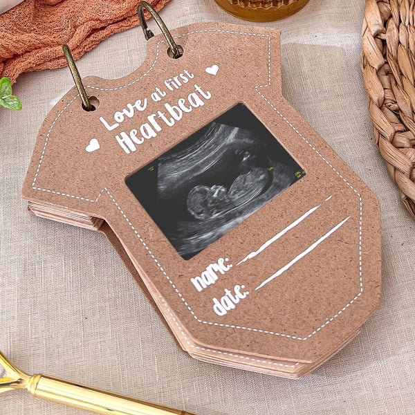 Brown photo album with ultrasound image and 'Love at first heartbeat' text on a textured surface.