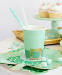 Green paper cup with gold accents on a decorative plate with polka dots and a straw.