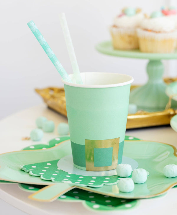 Green paper cup with gold accents on a decorative plate with polka dots and a straw.