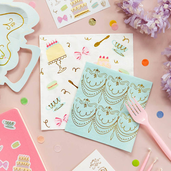 Decorative napkins with gold designs on a pink surface with stationery items.