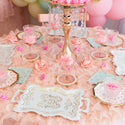 Decorative table setting with pink and gold elements, including a cake stand and floral arrangements.