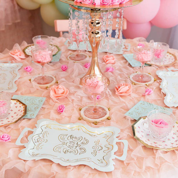 Decorative table setting with pink and gold elements, including a cake stand and floral arrangements.