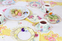 Tea party setup with floral tablecloth, plates, and teacups.