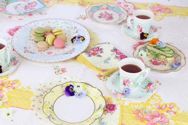 Tea party setup with floral tablecloth, plates, and teacups.