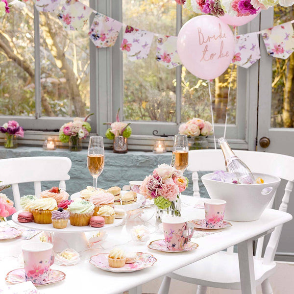Decorated table with pastel colors, balloons, and floral arrangements in a bright room.