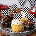 Cupcakes with checkered flags on a metal tray, with race car and checkered flag decorations in the background.