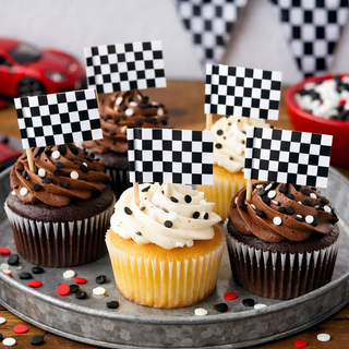 Cupcakes with checkered flags on a metal tray, with race car and checkered flag decorations in the background.