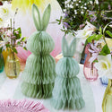 Two green paper bunny decorations on a table with floral arrangements.