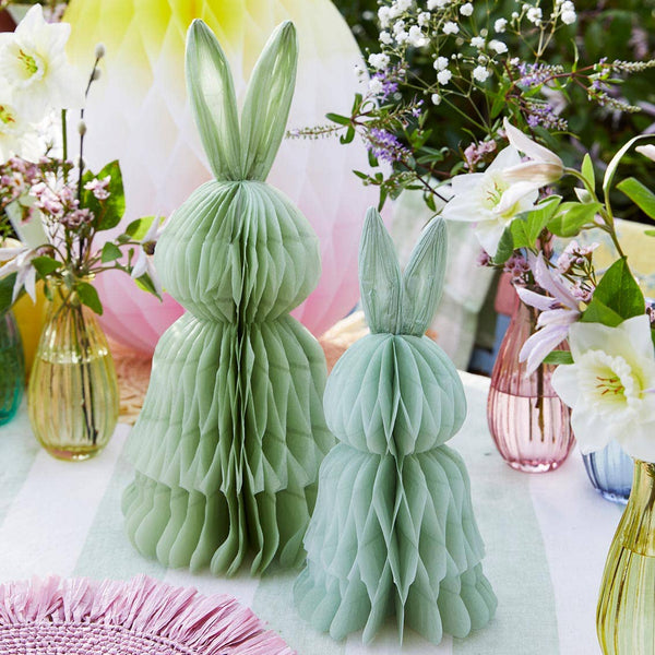 Two green paper bunny decorations on a table with floral arrangements.