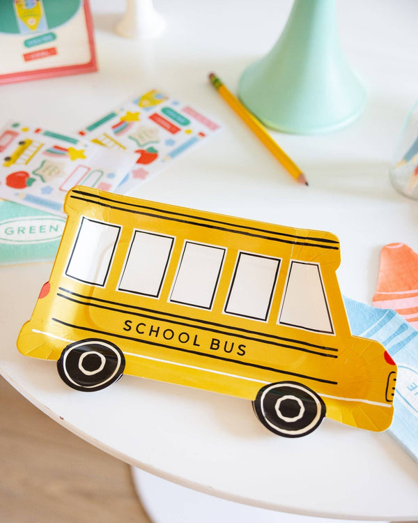 Yellow school bus-shaped pencil case on a white surface with educational materials in the background