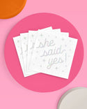 Stack of white napkins with 'she said yes!' text on a pink background