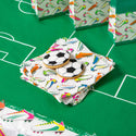 Cookies shaped like soccer balls and cleats on a colorful packaging with sports-themed design on a green surface.