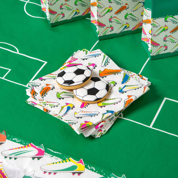 Cookies shaped like soccer balls and cleats on a colorful packaging with sports-themed design on a green surface.