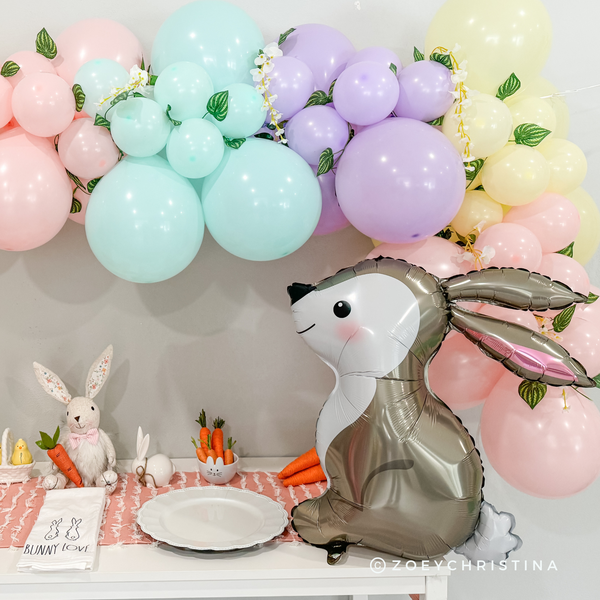 Decorative setup with pastel balloons, a rabbit-shaped balloon, and small rabbit figurines on a table.