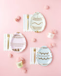 Easter-themed table setting with egg-shaped plates, pink and gold accents on a pink background.