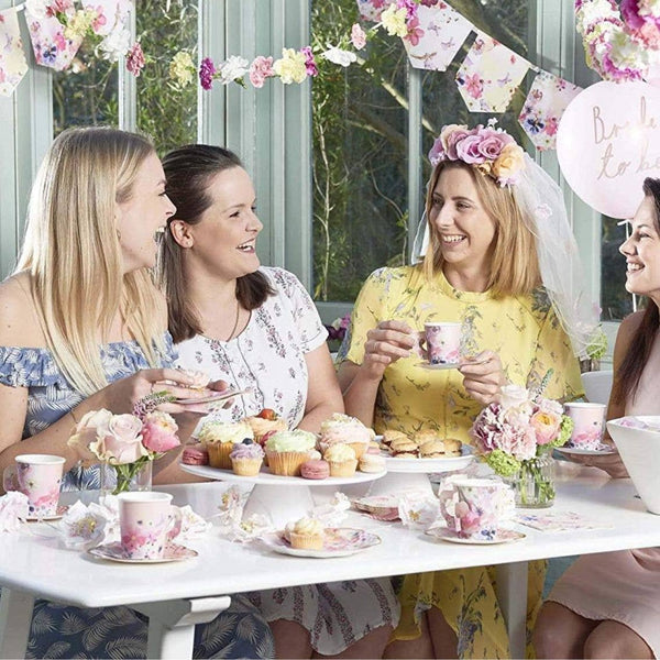 Four women enjoying a tea party with cupcakes and flowers in a garden setting.