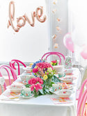 Tea party setup with floral centerpieces, balloons, and 'love' balloon in a celebratory setting.