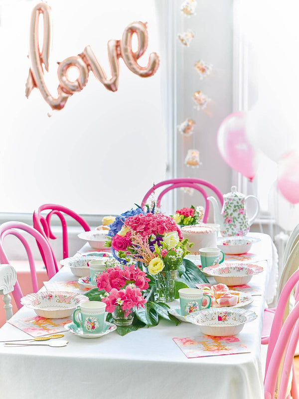 Tea party setup with floral centerpieces, balloons, and 'love' balloon in a celebratory setting.