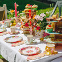 Decorative tea party setup with teacups, plates, and pastries on a table outdoors.