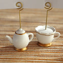 White ceramic teapot and teacup with gold accents on a textured surface