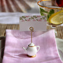 Teapot-shaped place card holder with a card on a pink napkin