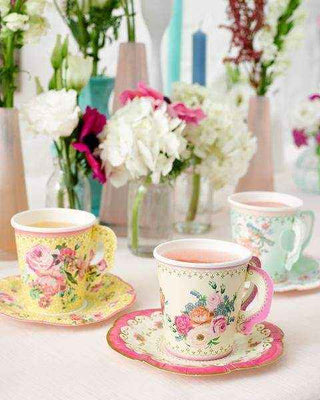 Decorative floral teacups and saucers on a table with flowers in the background