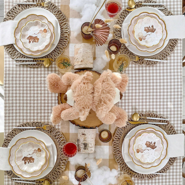 Decorative table setting with plates, candles, and a teddy bear on a checkered tablecloth.