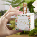 Hand holding a small box with a bear figurine on top, against a blurred green background