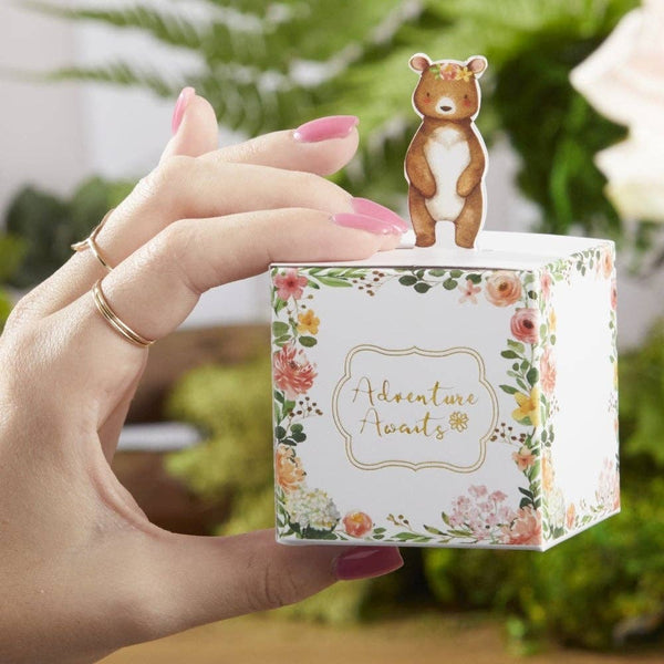 Hand holding a small box with a bear figurine on top, against a blurred green background