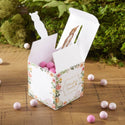 Decorative gift box with pink balls on a wooden surface with greenery in the background