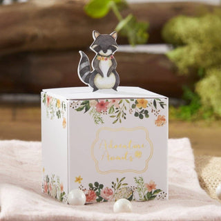 Decorative box with floral design and raccoon figurine on top, set against a blurred natural background.